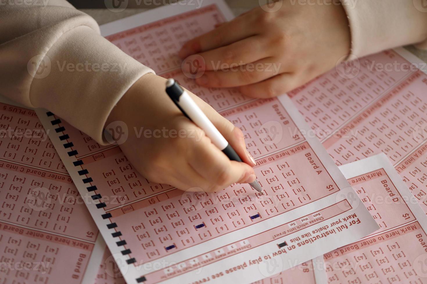 Filling out a lottery ticket. A young woman plays the lottery and dreams of winning the jackpot. Female hand marking number on red lottery ticket photo