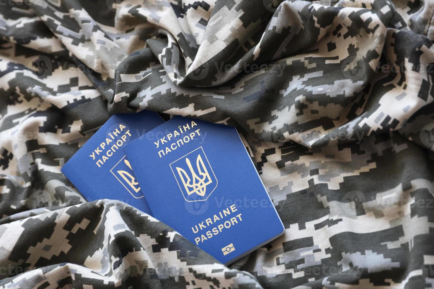 Ukrainian foreign passport on fabric with texture of military pixeled camouflage. Cloth with camo pattern in grey, brown and green pixel shapes and Ukrainian ID photo