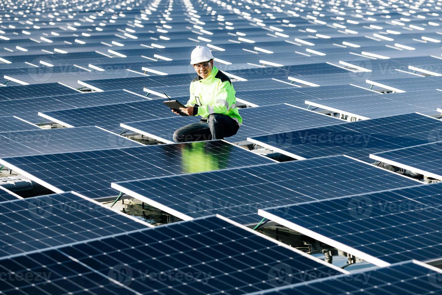 retrato de un trabajador sonriente, instalando baterías solares, que está parado en una escalera en una planta solar contra el cielo azul, mostrando el pulgar hacia arriba. concepto de fuentes alternativas de energía. foto