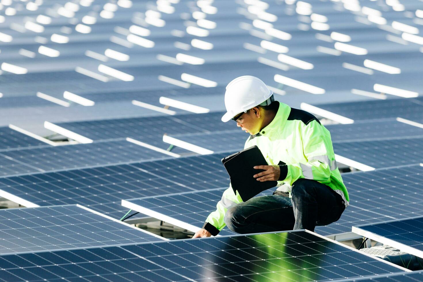 Closed-up of Male electrician in white safety helmet standing on ladder and mounting photovoltaic solar panel under beautiful blue sky. Concept of alternative sources of energy. photo