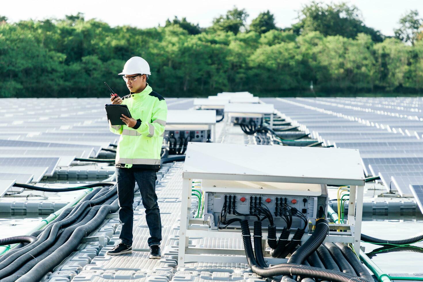 Male electrician in white safety helmet standing on ladder and mounting photovoltaic solar panel under beautiful blue sky. Concept of alternative sources of energy. photo