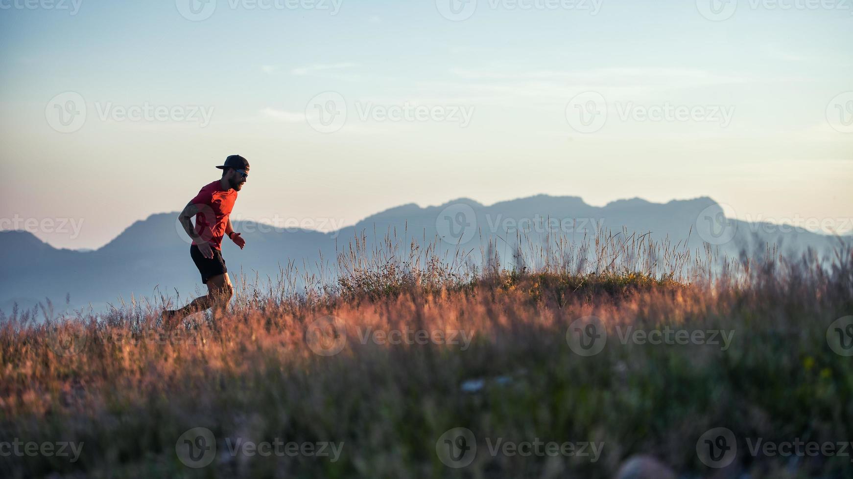 A young sportsman runs at sunset in the hills photo