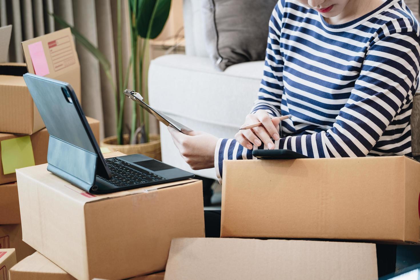 Online selling business idea, beautiful girl checking the products that customers ordered on their mobile phones and tablet  in order to pack the products into parcel boxes to deliver to customers. photo