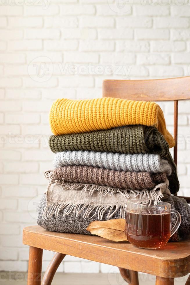 Stack of autumn warm sweaters on old wooden chair, white brick wall background photo