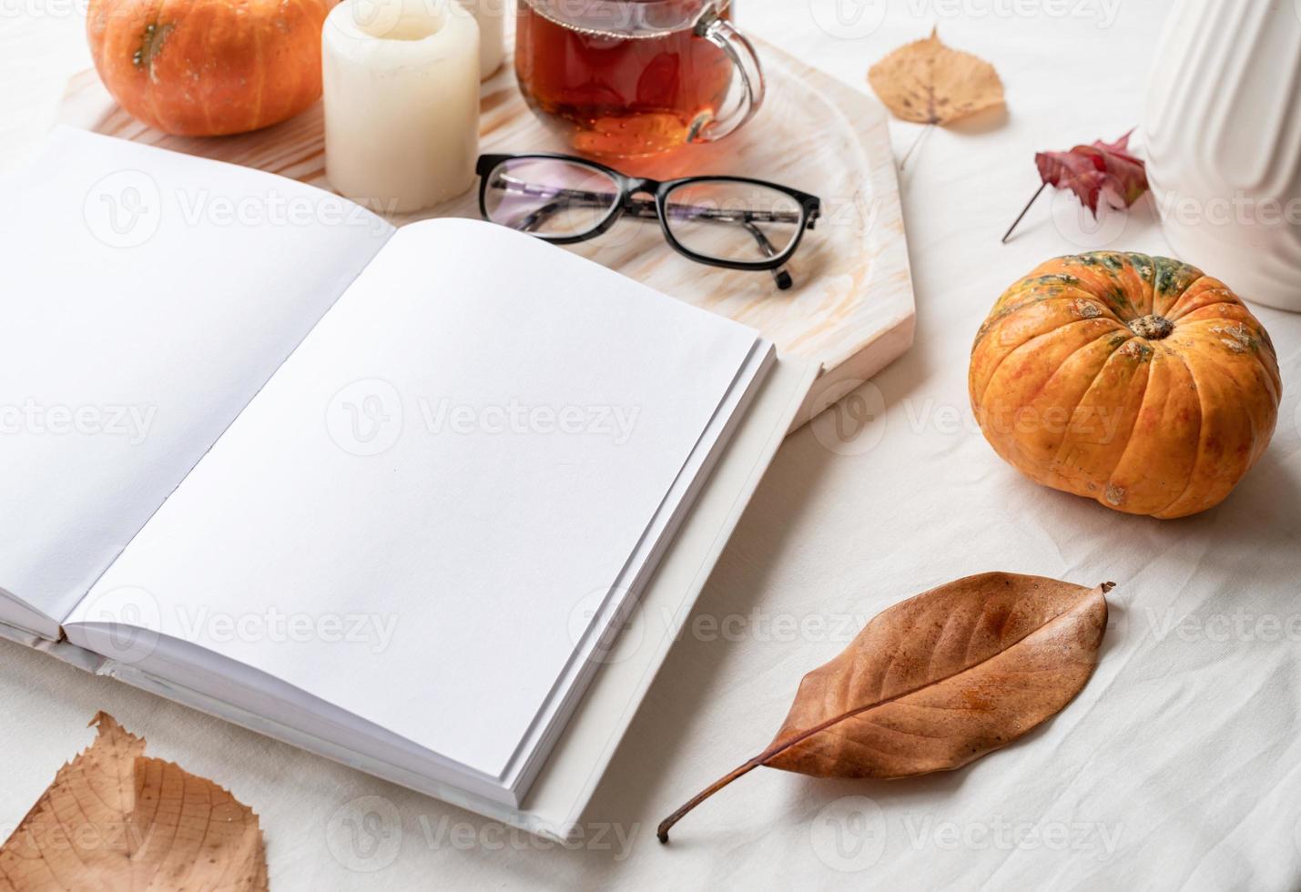 white blank book with autumn leaves, glasses and candles on white table , mockup design photo