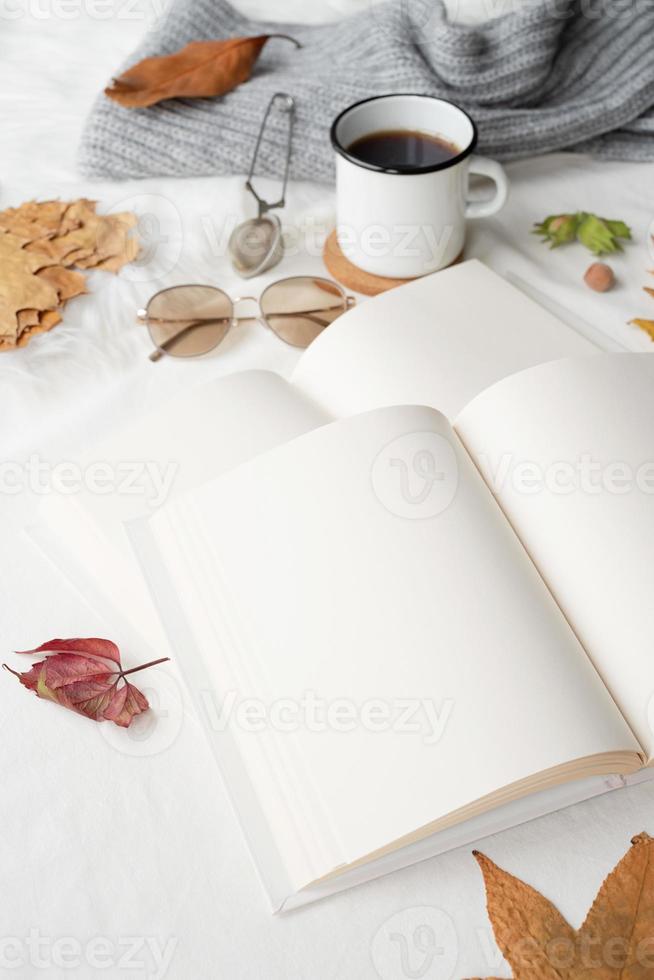 white blank book with autumn leaves and cup of hot tea on old table , mockup design photo