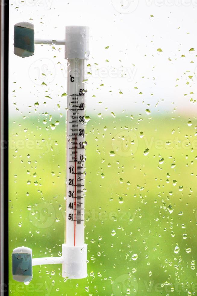 window glass with rain drops and thermometer photo