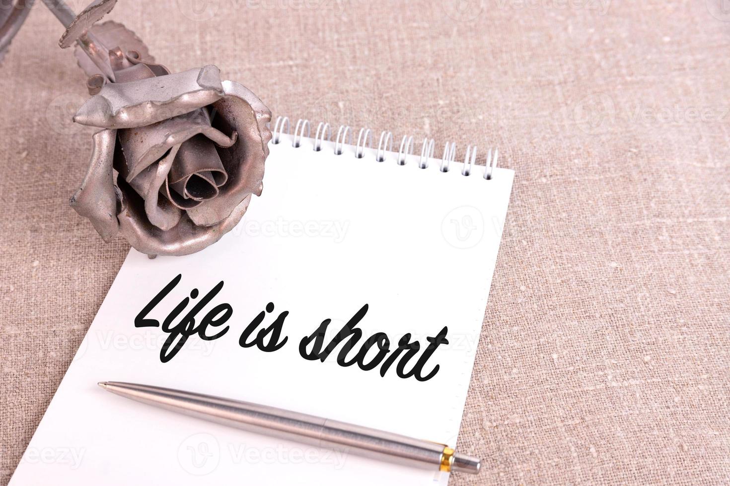 Life is short, the text is written in a notebook lying on a linen linen and an iron rose flower. photo