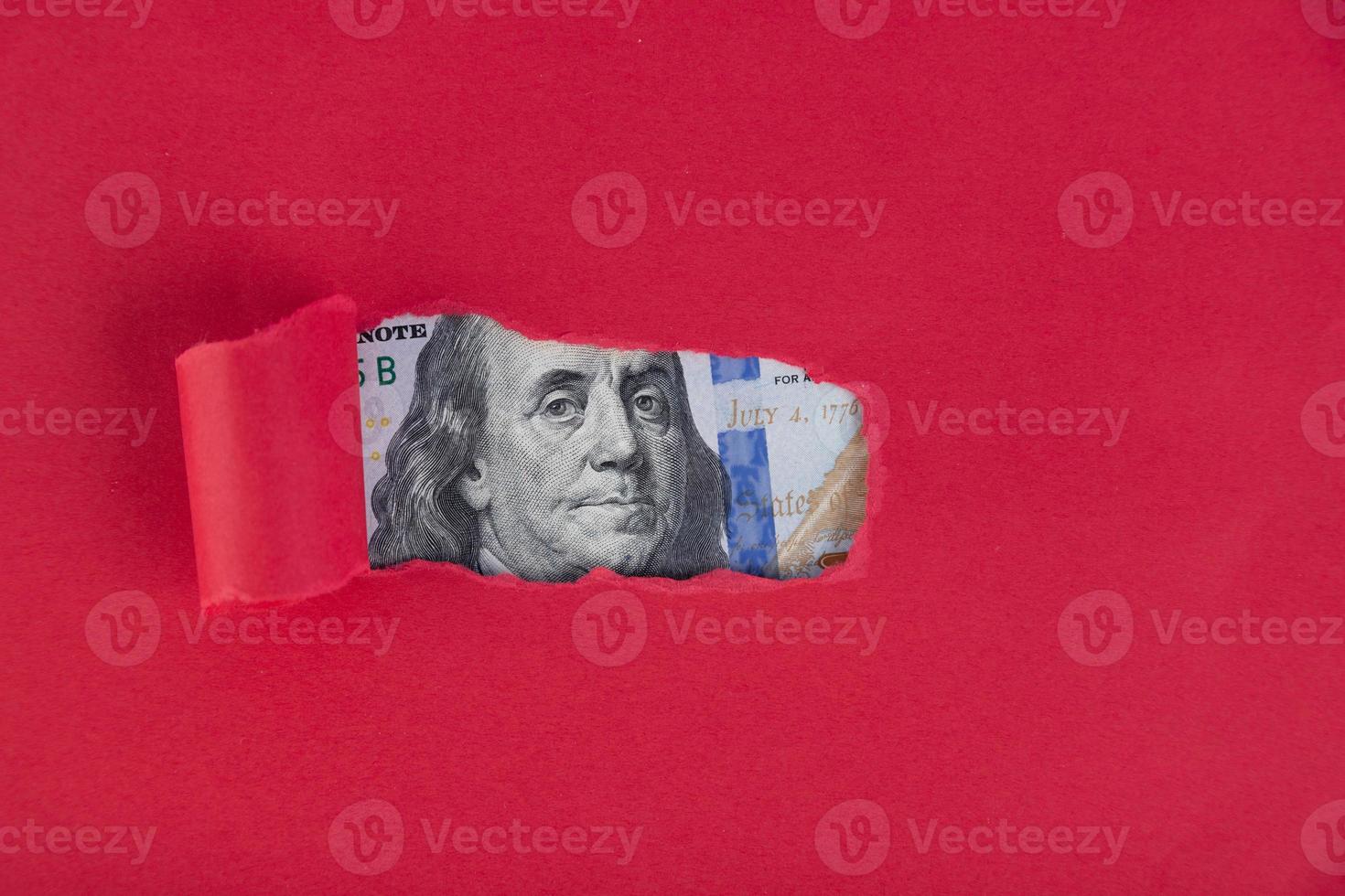 un fondo rojo, bajo el cual asoma un retrato representado en un billete de cien dólares. foto