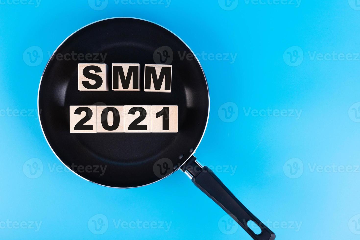 palabra smm 2021, texto escrito en cubos de madera, bloques de construcción sobre una sartén y fondo azul. foto