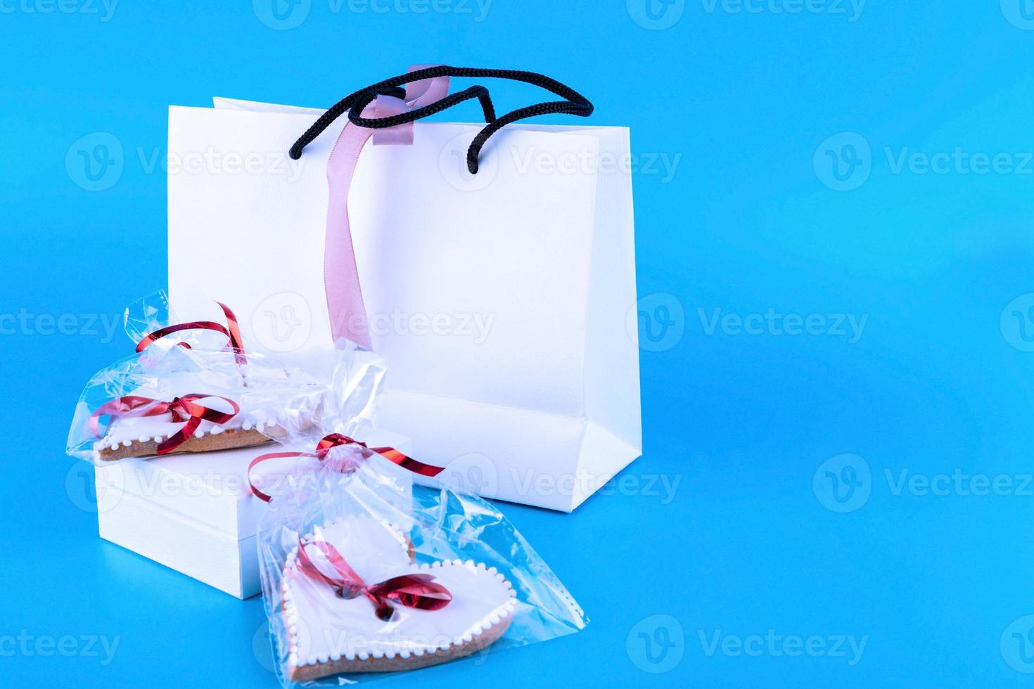 Valentine's Day cookies. Sweet heart-shaped cookies and white paper bag. Homemade baking. View from above. Blue background. Copy space. photo
