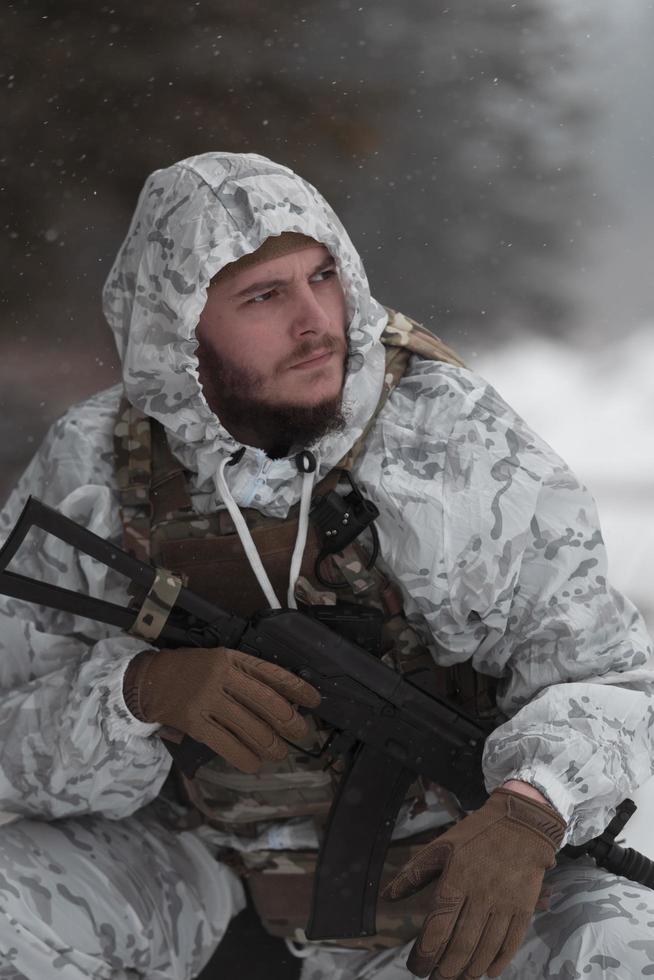 Winter war in the Arctic mountains. Operation in cold conditions.Soldier in winter camouflaged uniform in Modern warfare army on a snow day on forest battlefield with a rifle. Selective focus photo