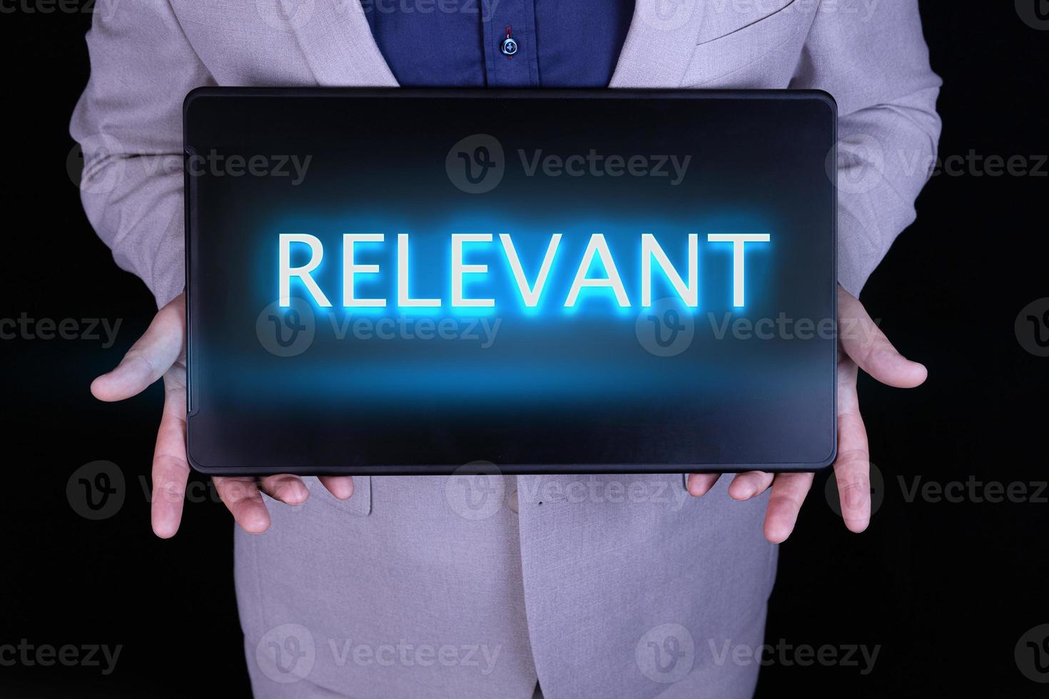 RELEVANT text, word written in neon letters on a black laptop, in front of a businessman in a gray suit. photo