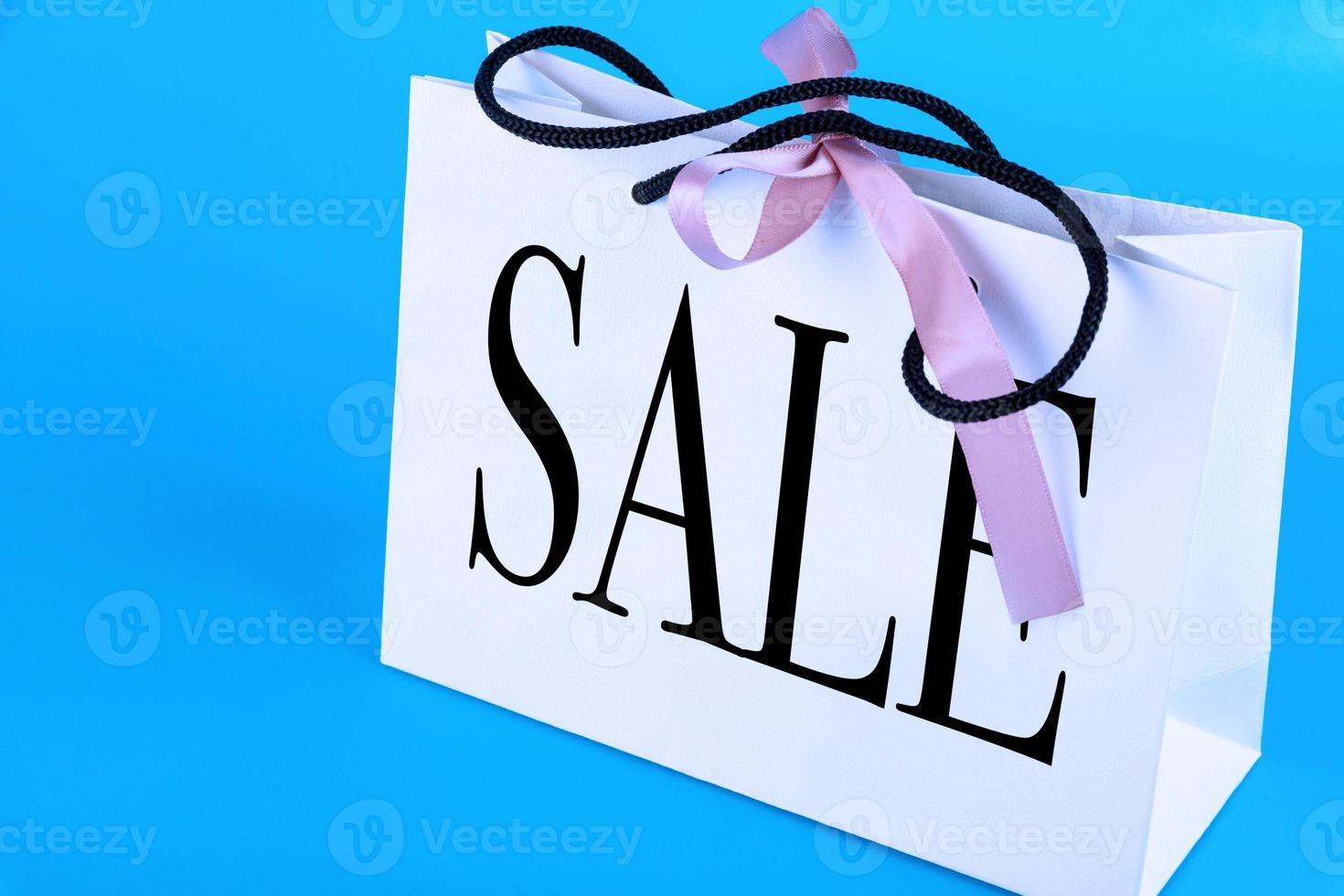 White paper bag, shopping bag with text, the inscription SALE on a blue background. Copy space. photo