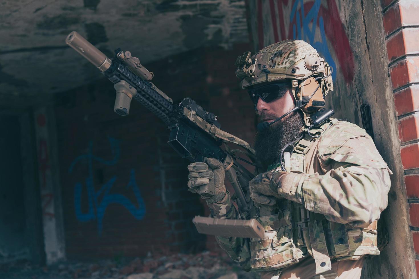 un soldado barbudo con uniforme de las fuerzas especiales en una peligrosa misión militar, vuelve a archivar su arma mientras se esconde de la pared. enfoque selectivo foto