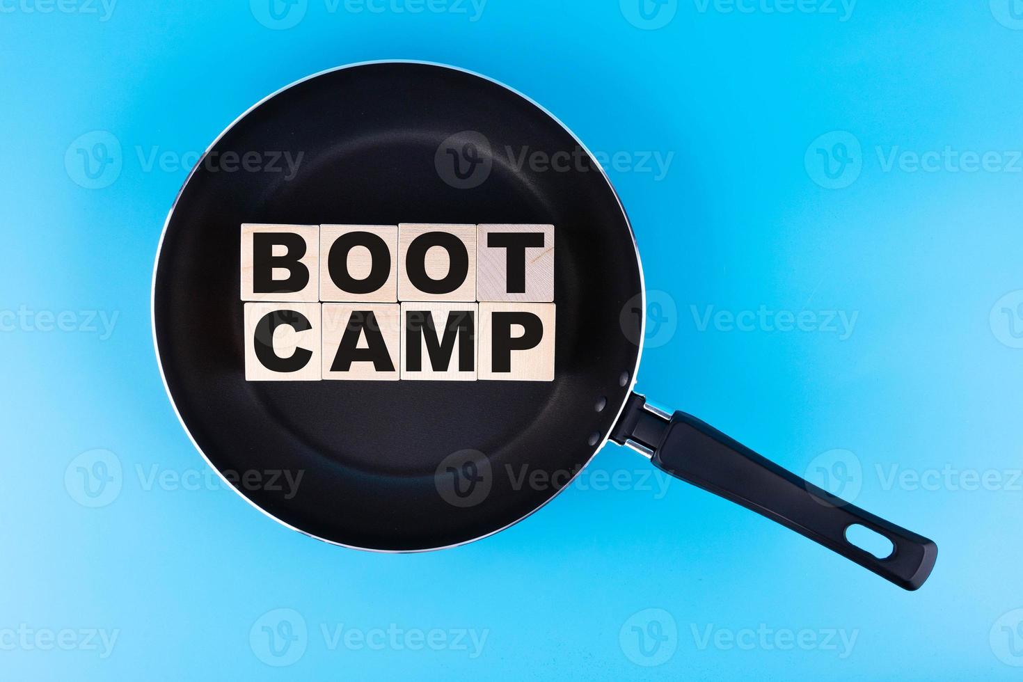 BOOTCAMP word, text written on wooden cubes, building blocks lying on a frying pan and a blue background. photo