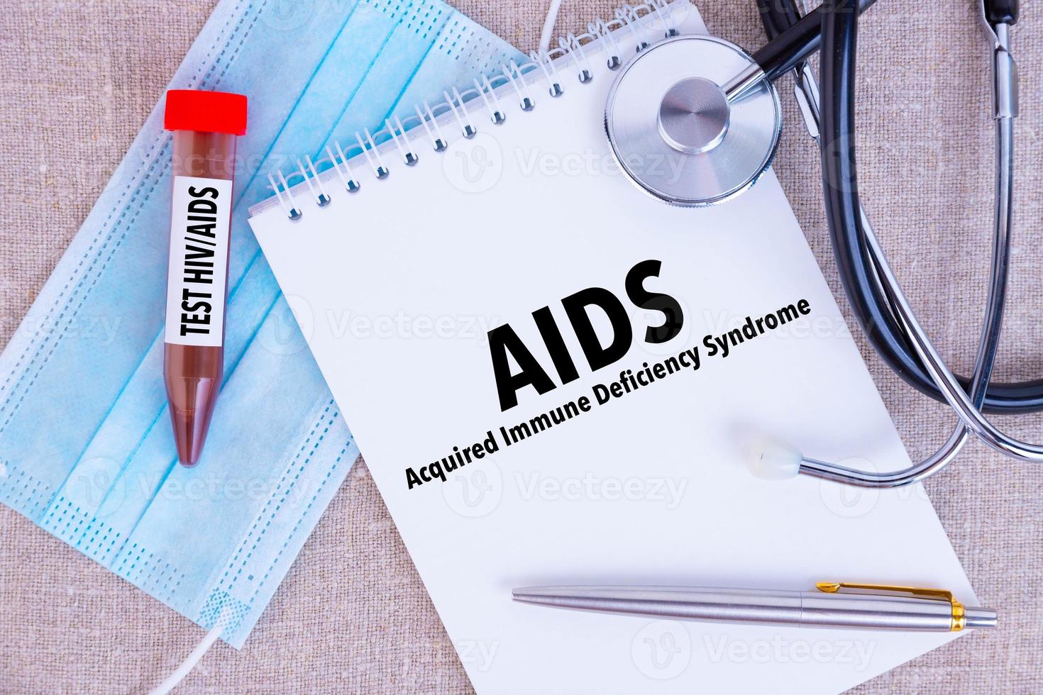 AIDS Acquired Immune Deficiency Syndrome, the text is written in a notebook, next to a pen, a disposable medical mask stethoscope on a linen background photo