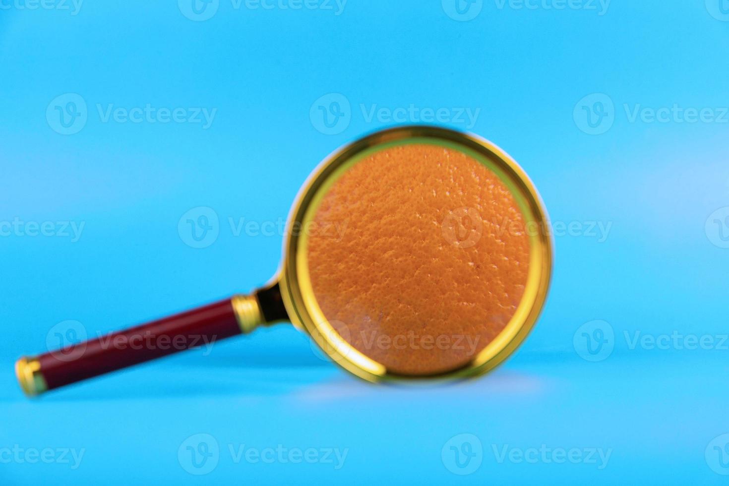 Magnifying glass and orange on a blue background as a symbol of cellulite. Concept Anti-cellulite program. photo