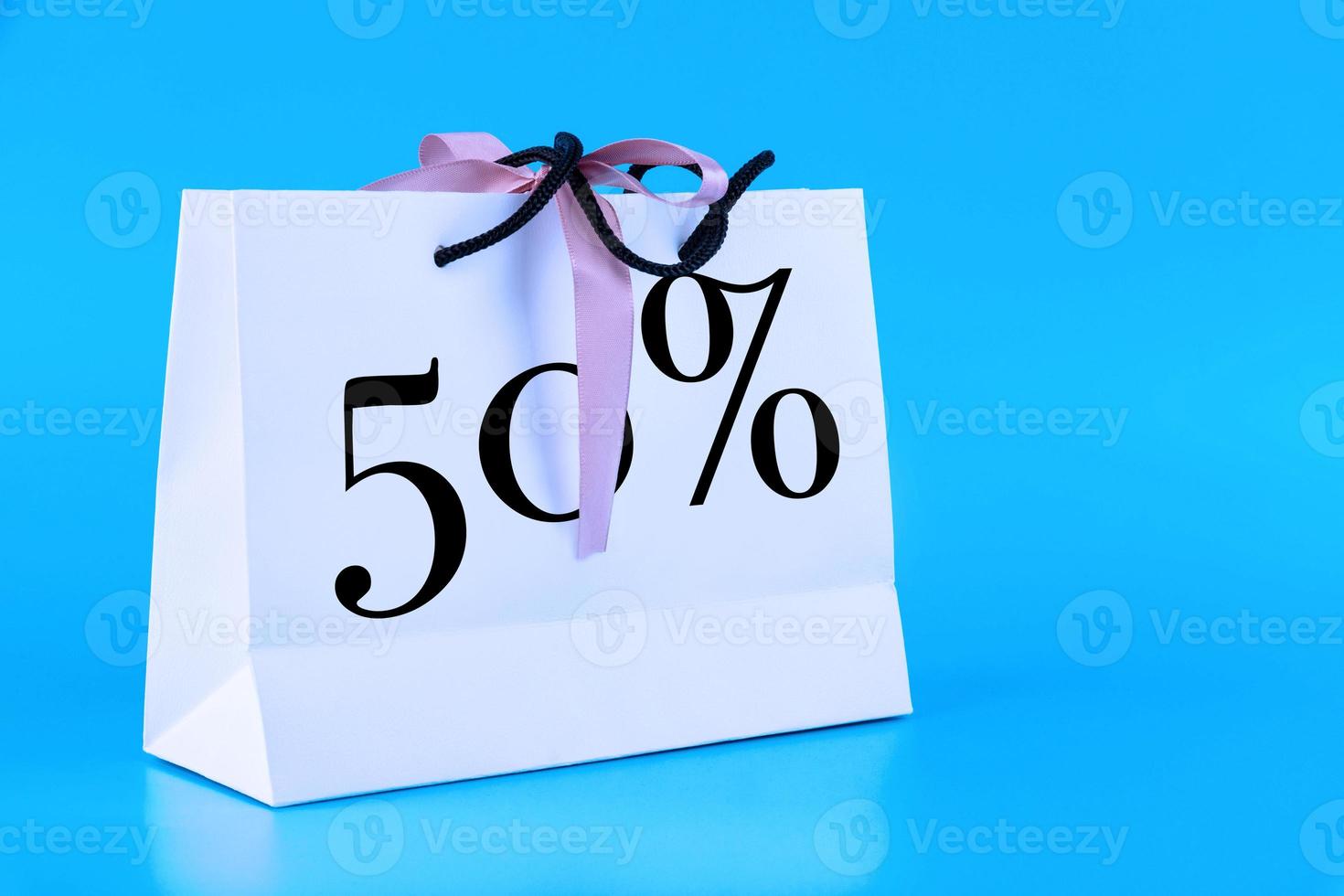 White paper bag, shopping bag with 50 percent sign on blue background. Copy space. photo