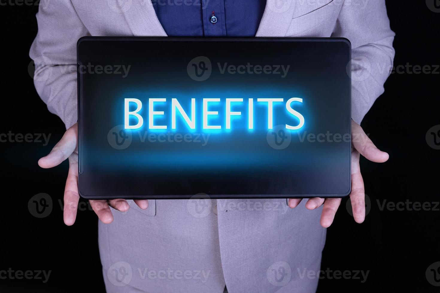 BENEFITS text, word written in neon letters on a black laptop, in front of a businessman in a gray suit. photo