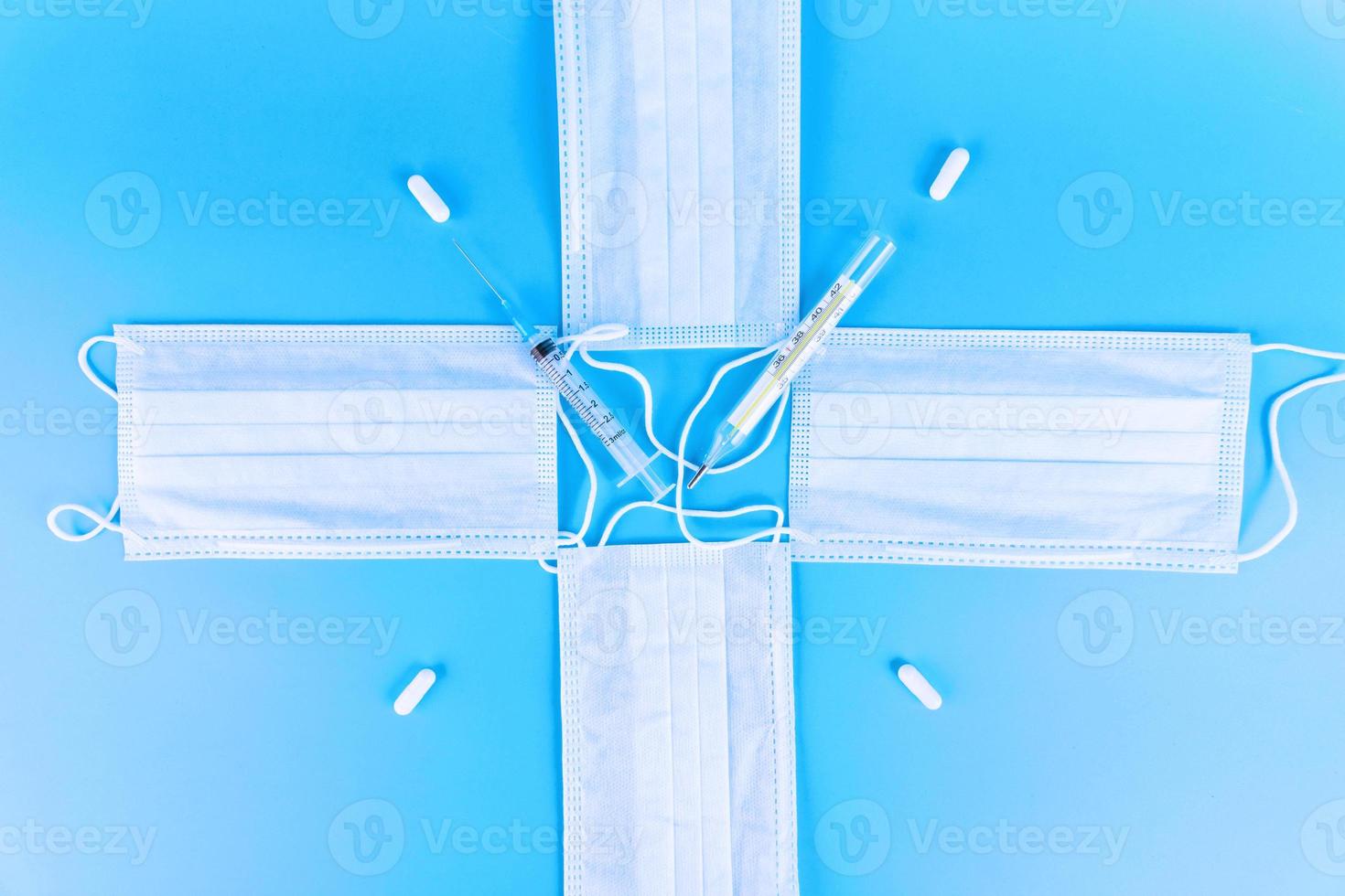 Disposable blue medical masks are folded in the form of a clock, in the form of a cross with a thermometer, a syringe and pills. photo