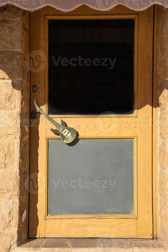 Wooden front door with glass, with a door handle in the form of a guitar. photo