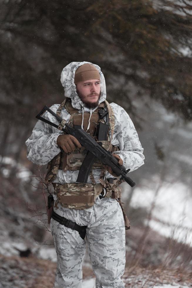 Winter war in the Arctic mountains. Operation in cold conditions.Soldier in winter camouflaged uniform in Modern warfare army on a snow day on forest battlefield with a rifle. Selective focus photo