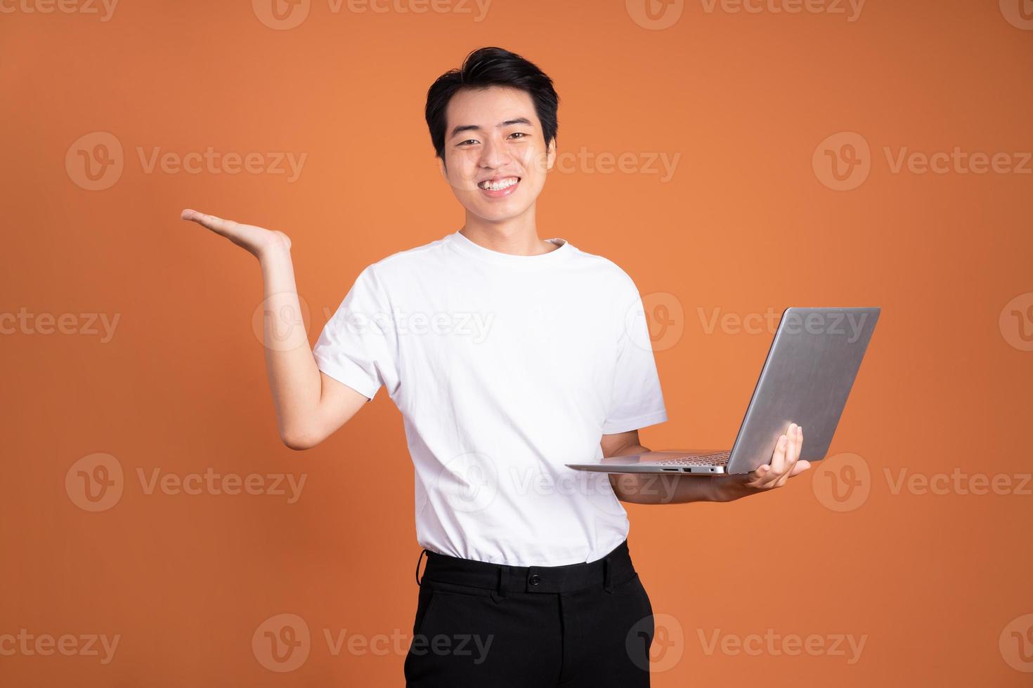 hombre asiático sosteniendo un portátil, aislado de fondo naranja foto