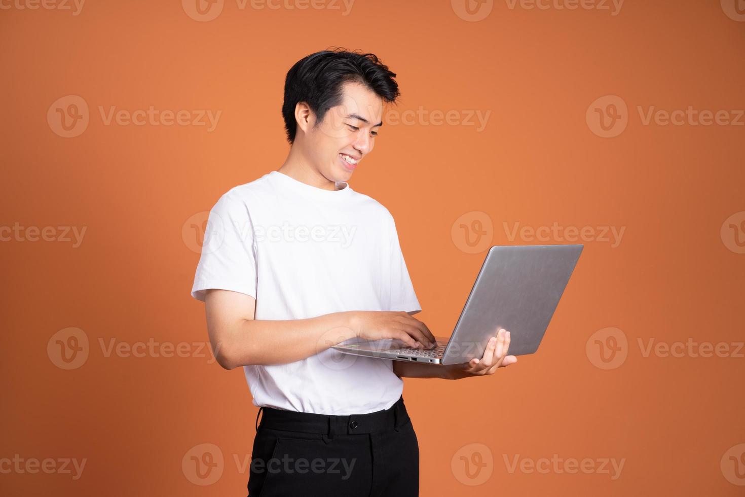 asian man holding laptop, isolated on orange background photo