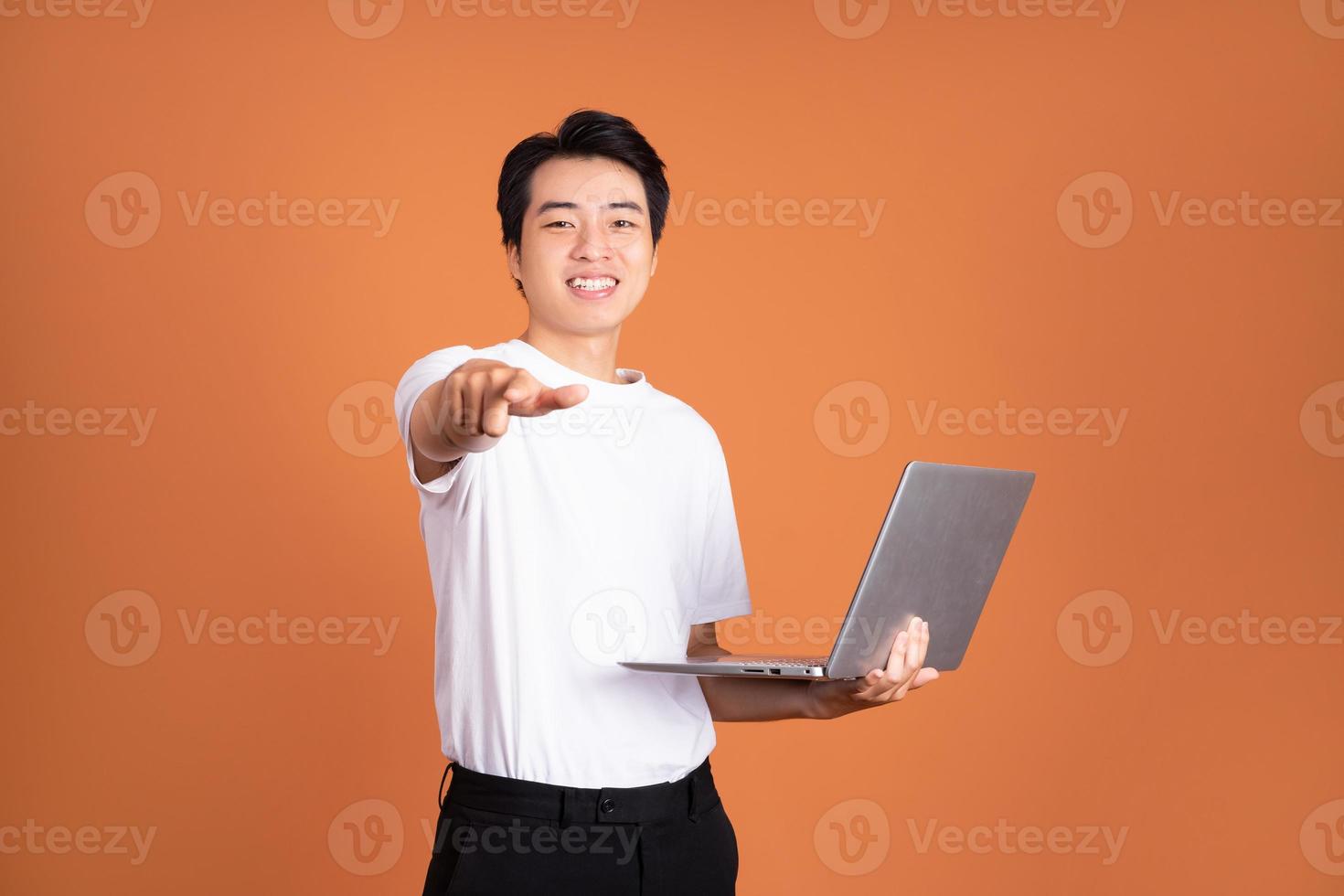 hombre asiático sosteniendo un portátil, aislado de fondo naranja foto