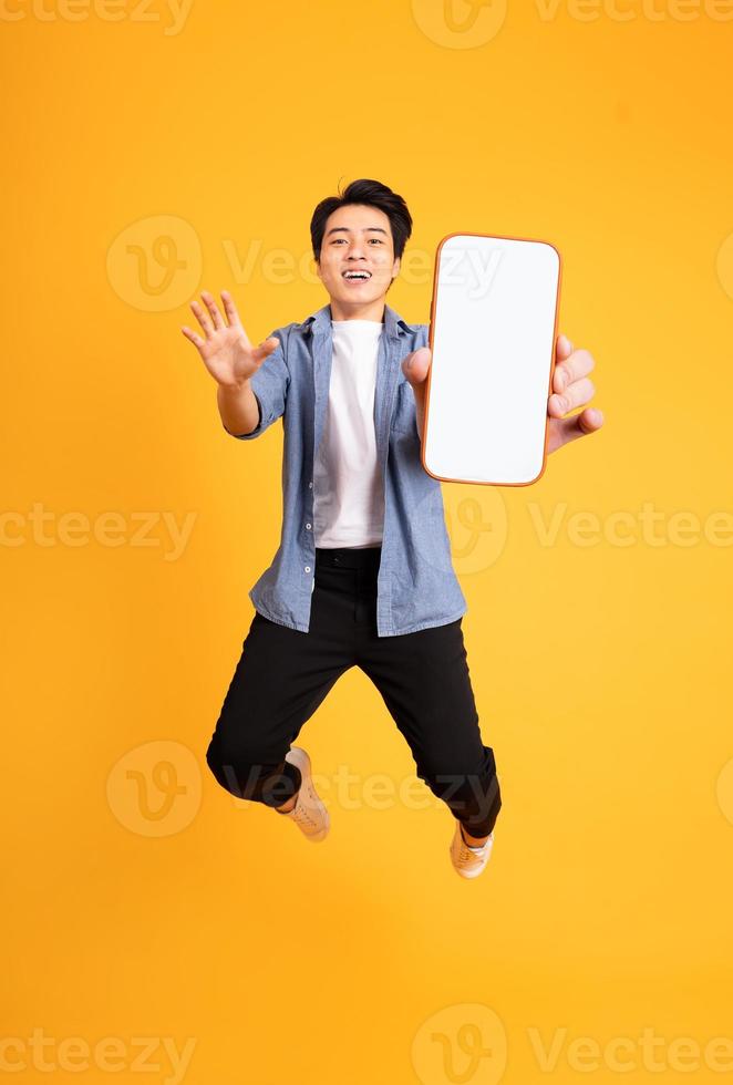 image of jumping up asian man holding smartphone in hand, isolated on yellow background photo