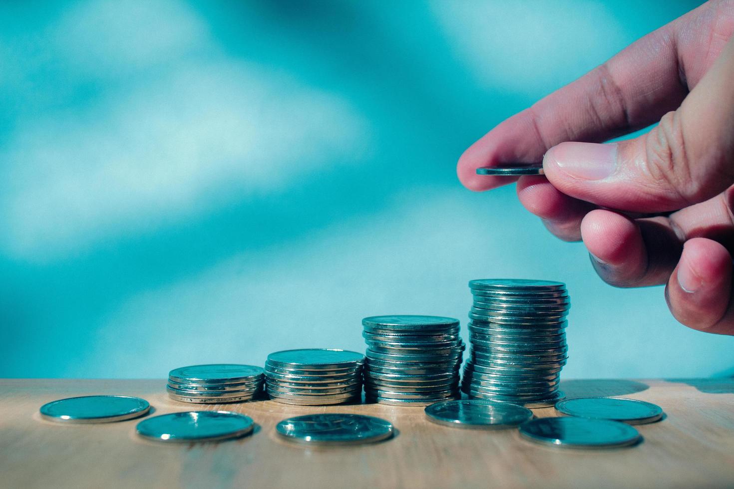 Man hand putting money to coins stack on wooden table with blurry background saving concept photo