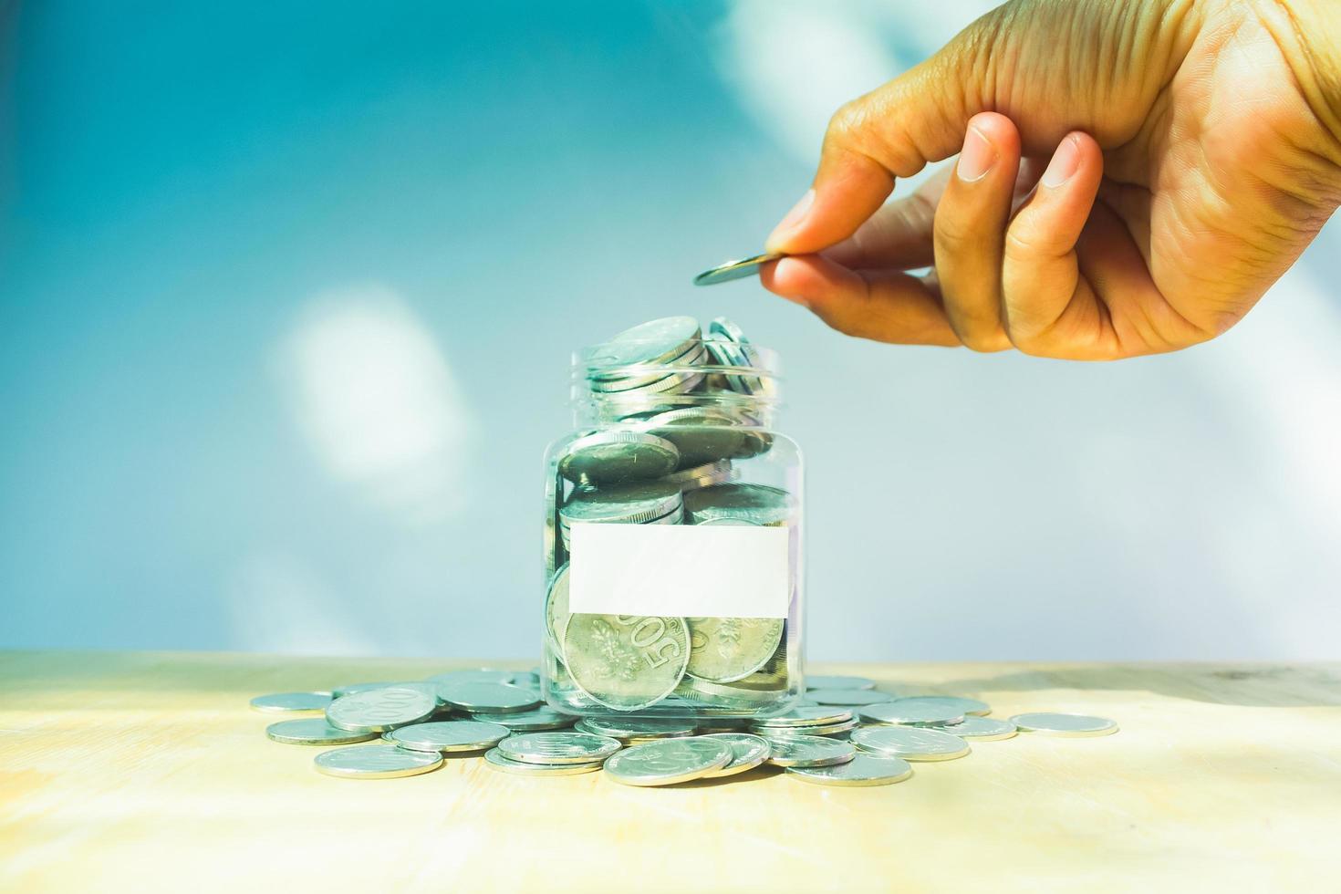 Man hand putting money to glass of coins on wooden table with blurry background saving concept photo