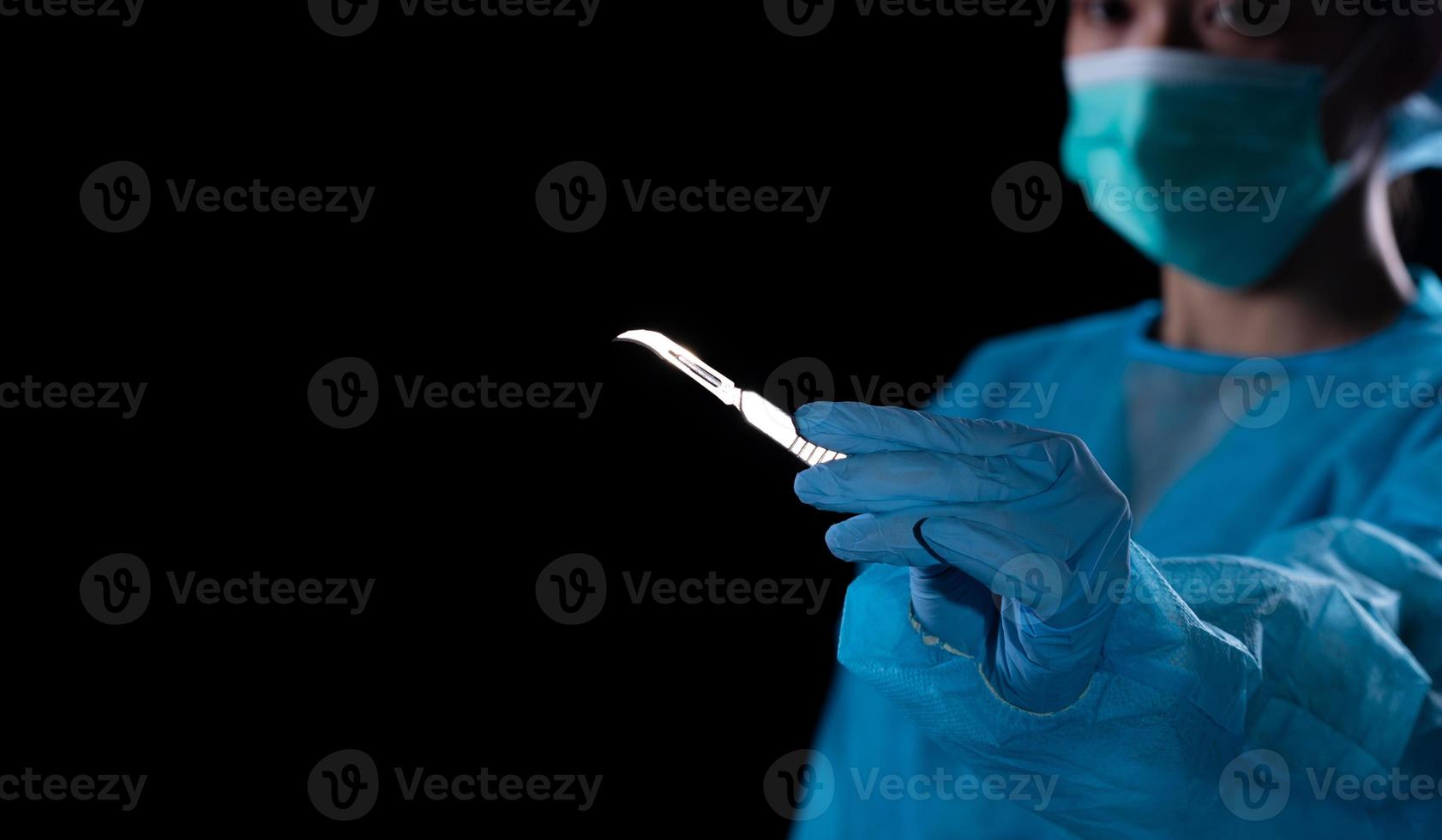 Hand of surgeon in blue medical glove holding a scalpel, express emotion feeling stress before operation. Tools medical instrument. Black background underexposure for shadow environment copy space photo