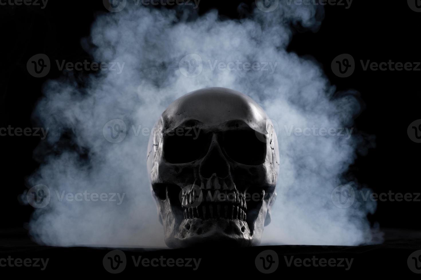 cráneo humano de halloween en una vieja mesa de madera sobre fondo negro. forma de hueso del cráneo para la cabeza de la muerte en el festival de halloween que muestra horror, miedo al diente malvado y miedo con humo de niebla, espacio de copia foto