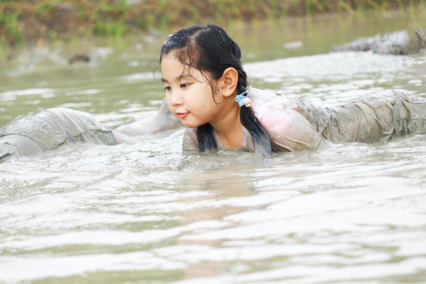 children having fun playing in the mud in the fields on a cloudy day. Asian children wade through water and dirty mud. Children's outdoor play and learning outside the classroom photo