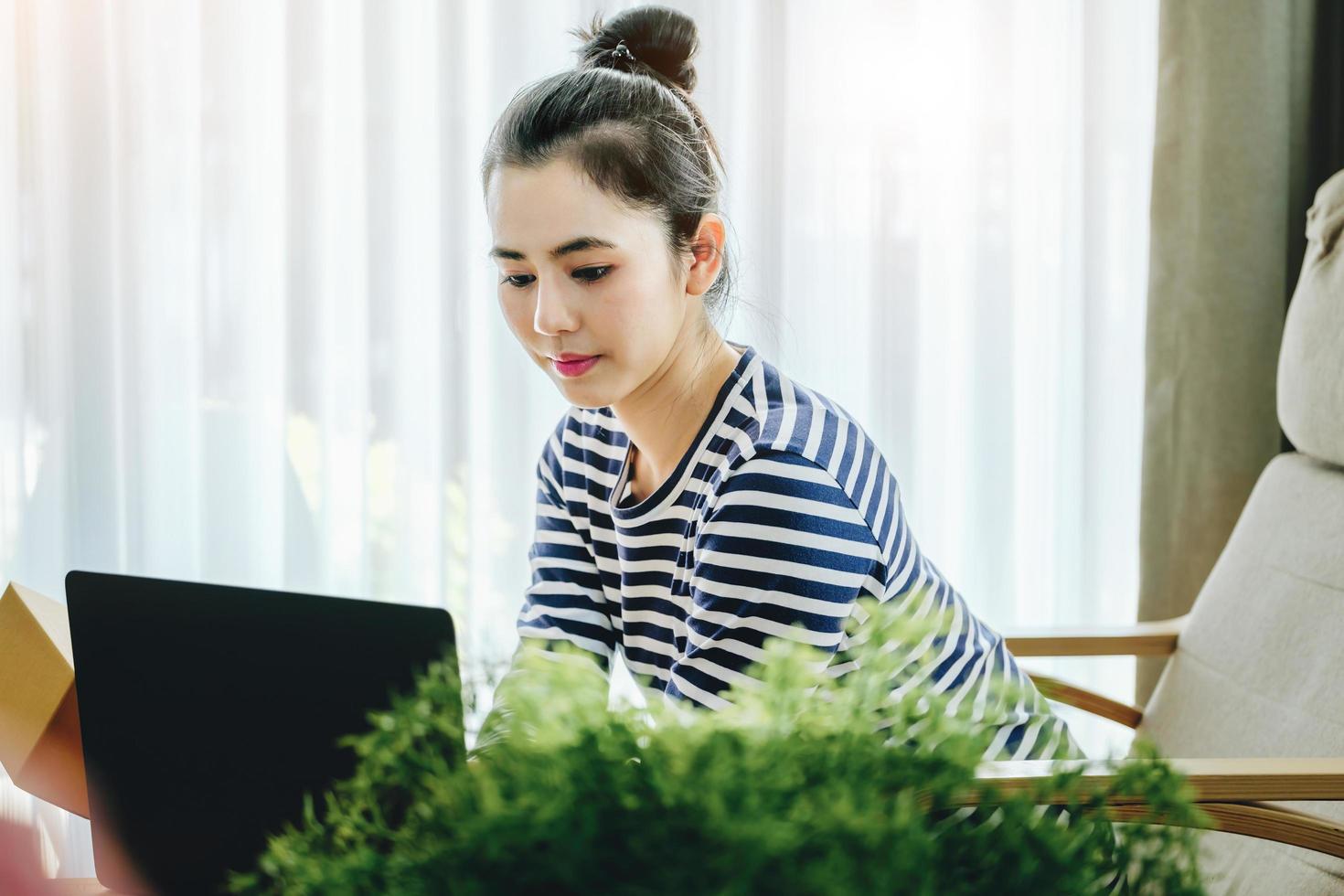 Online merchandising business idea, beautiful girl holding a parcel delivery box and using a computer to input Track And Trace parcel numbers to customers. photo