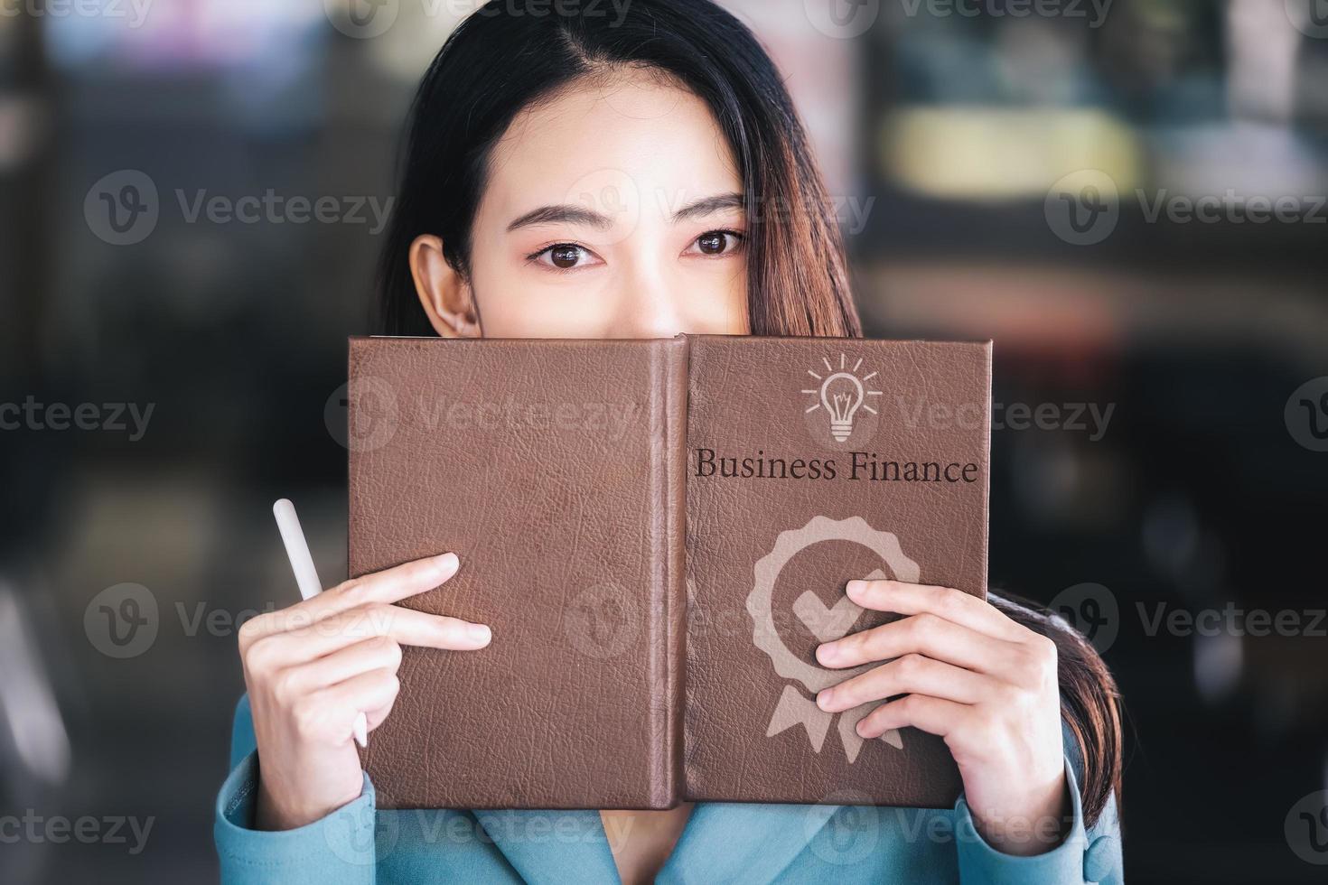 Asia woman entrepreneur or businesswoman showing a smiling face while reading a book developing financial and investing strategies. photo