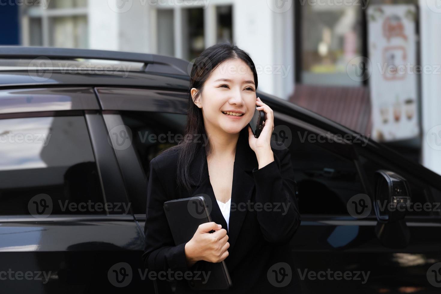 Asian businessmen, business owners, company presidents or female employees talking on the phone and holding a tablet are getting out of the car to attend a business plan meeting at the meeting. photo
