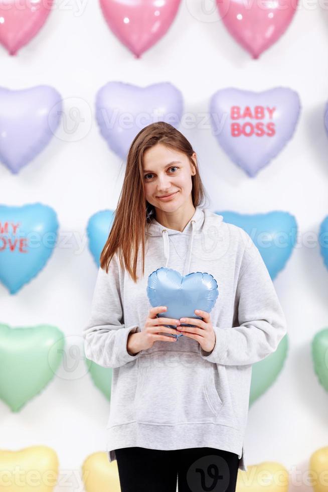 beautiful young woman holds the blue balloon in the form of a heart. many hearts background. valentines day. baby shower. selective focus photo