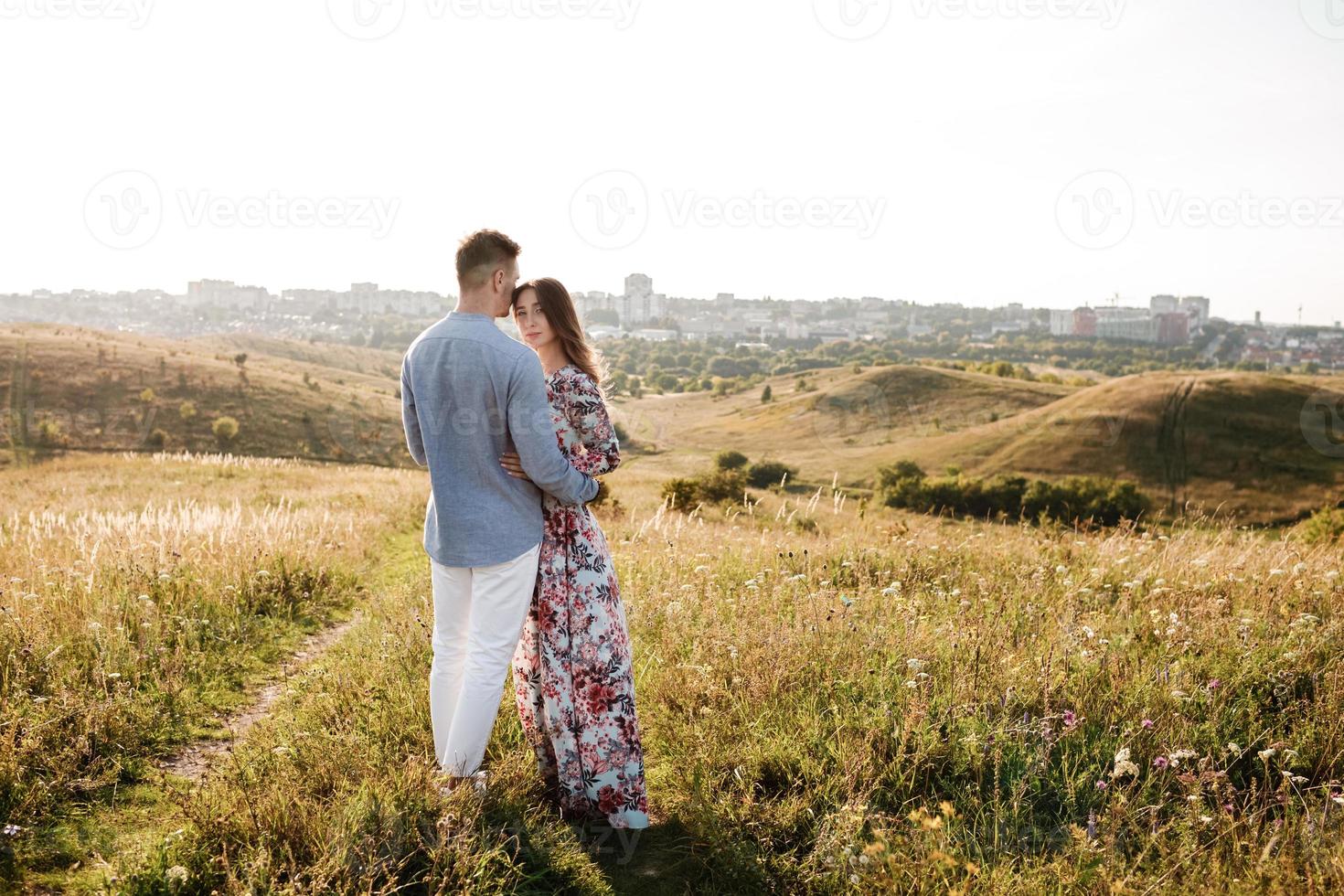 beautiful young couple hugging in a field with grass at sunset. stylish man and woman having fun outdoors. family concept. copy space. photo