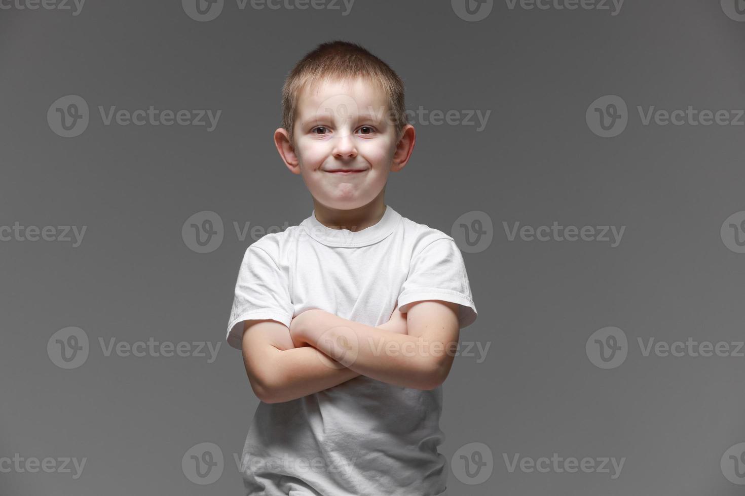 Portrait of happy little boy in white t-shirt smiling on gray background looking at camera in studio setting. Portrait of fashionable male child. photo