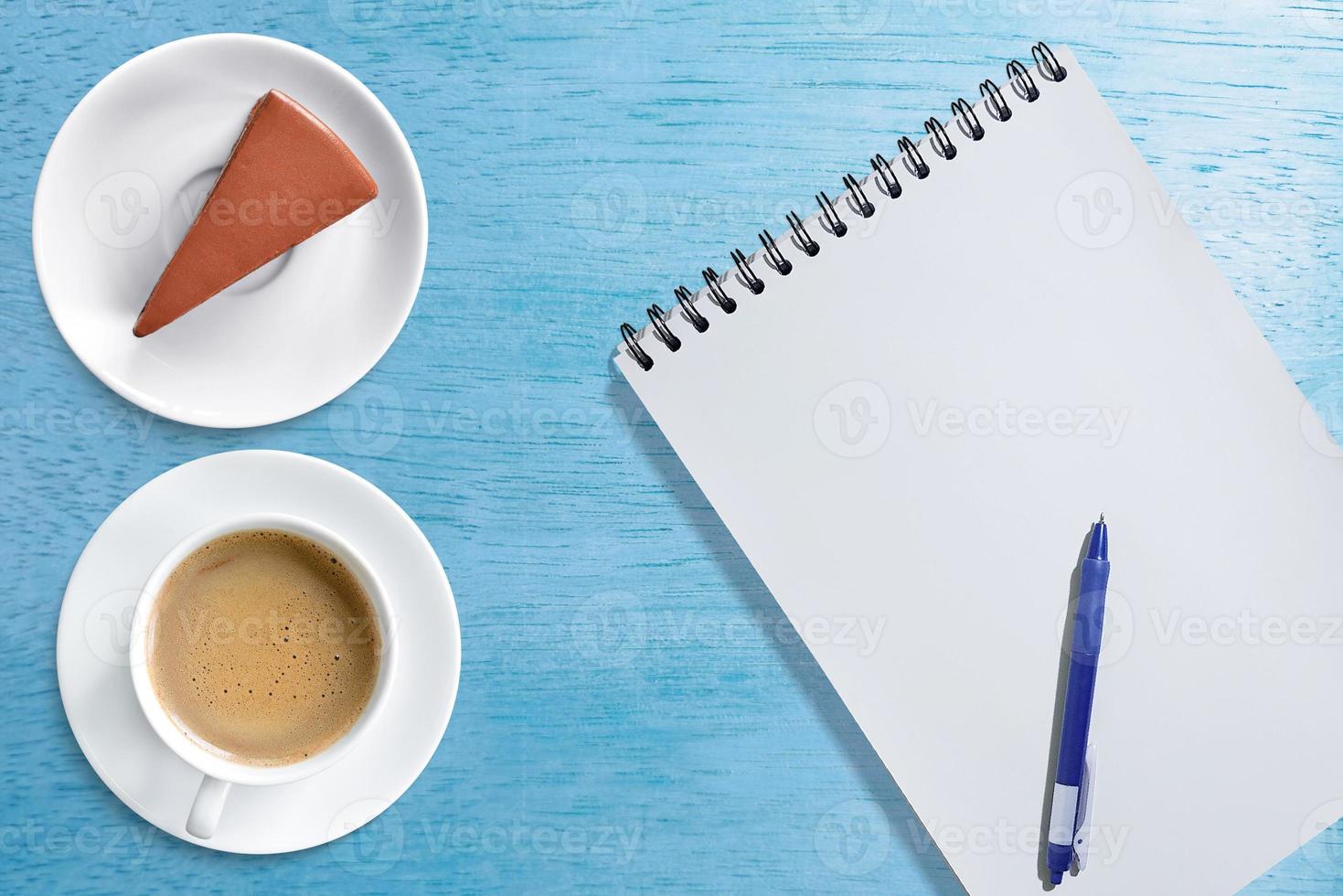 Coffee mug with chocolate cake Notebook with pen on top, top view, isolated on blue wooden table. photo