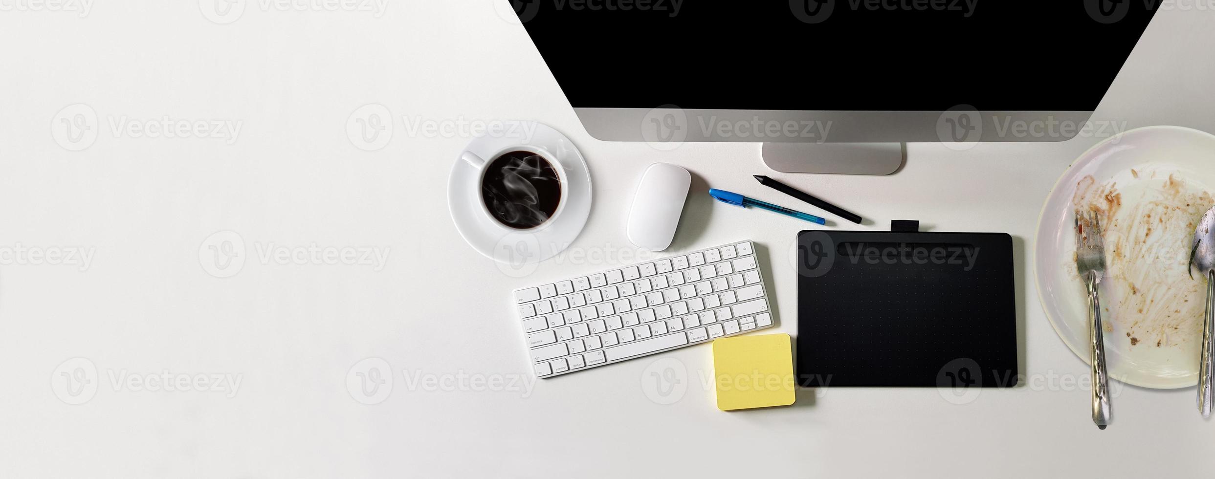 escritorio de oficina blanco moderno con computadora de pantalla negra, una taza de café, un cuaderno, un bolígrafo, un plato de comida que se ha comido. vista superior con espacio de copia, tumbado foto