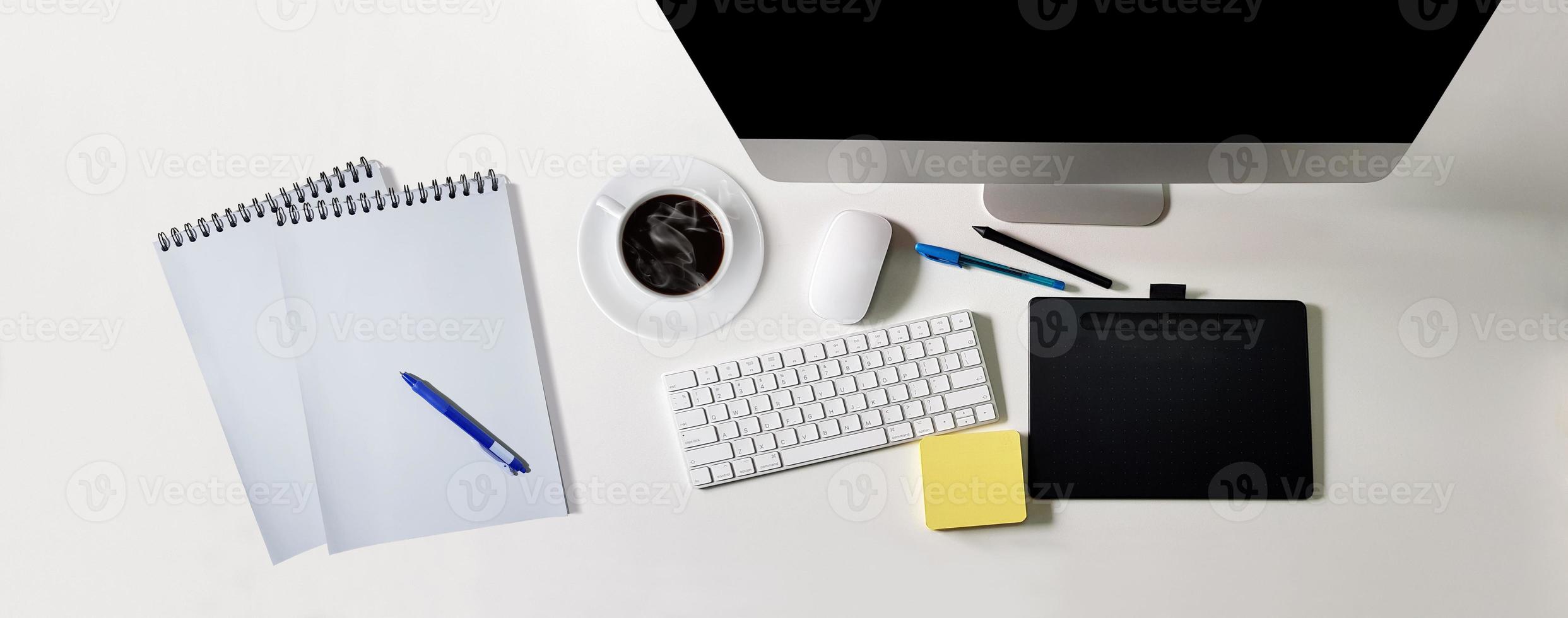 Modern white desk with black screen computer, coffee cup, notebook for writing messages, pens, top view photo