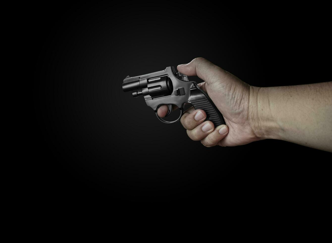 male hand holding a black revolver on a black background Criminals with handguns at close range Weapons for attack or defense photo