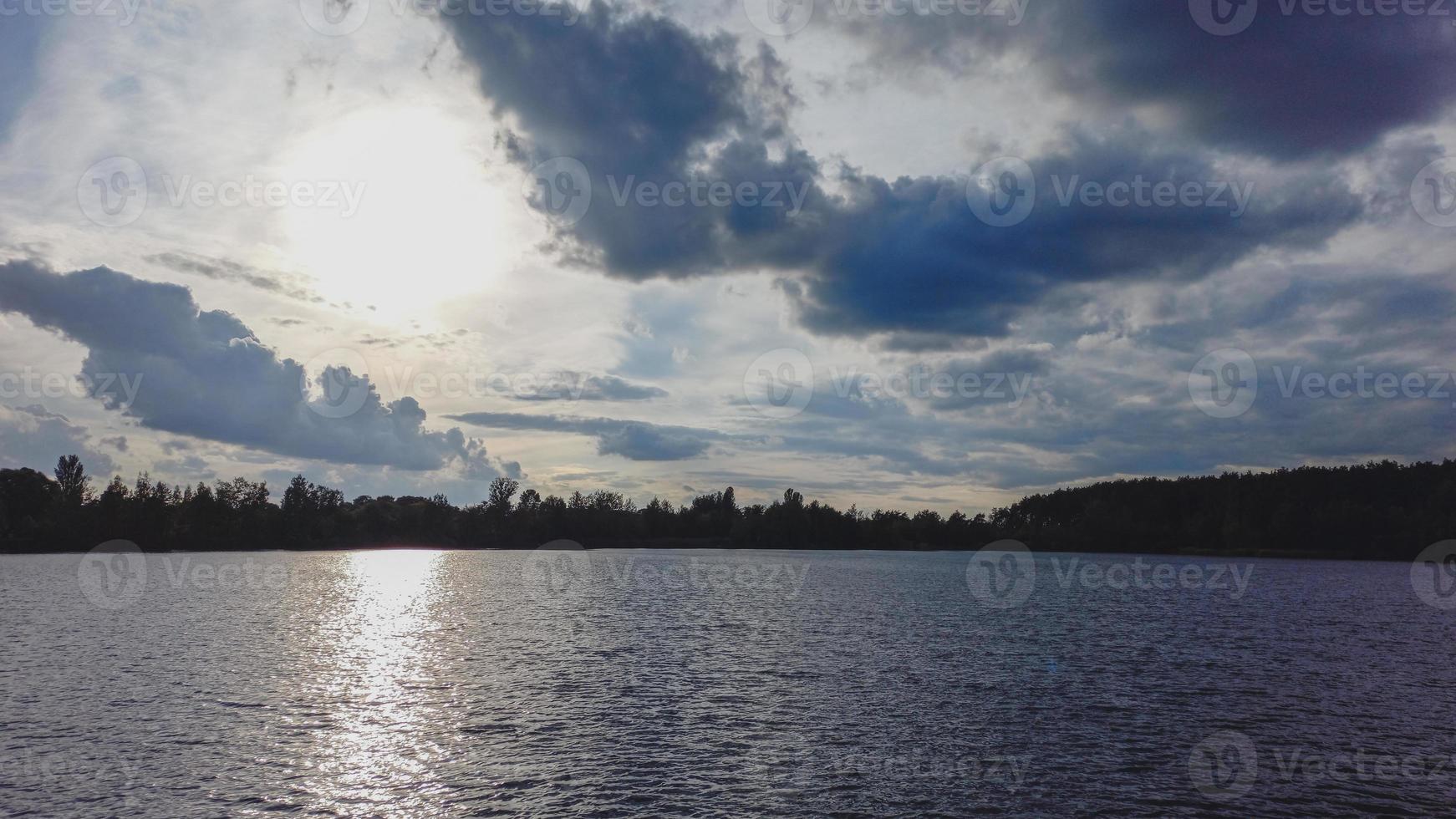 puesta de sol atmosférica detrás de los árboles y reflejo en el agua. foto