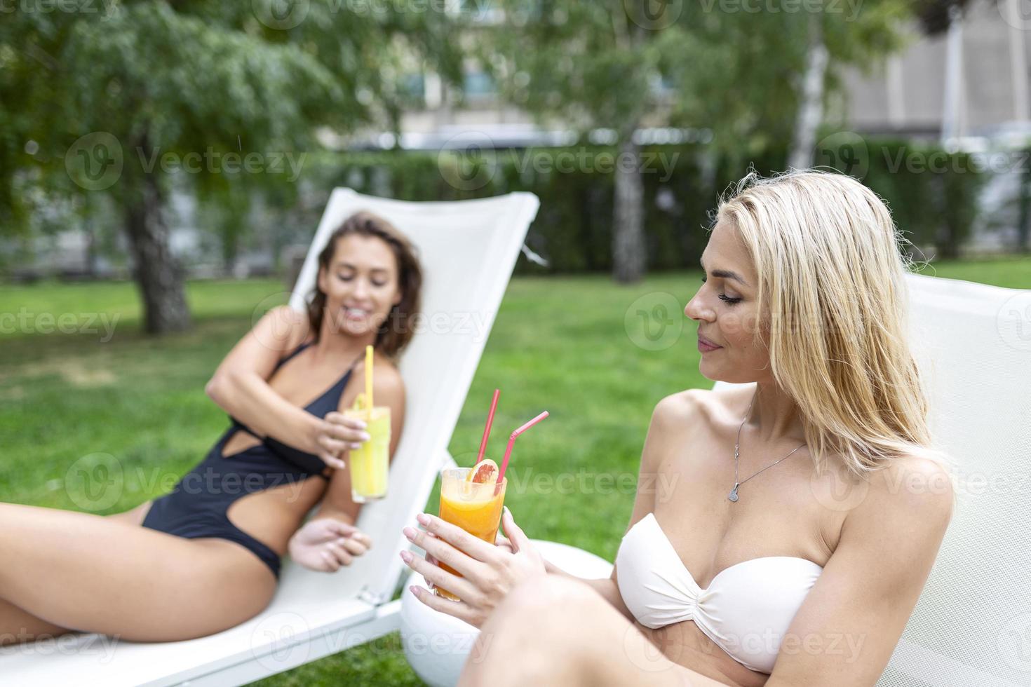 dos amigas en trajes de baño tomando el sol en las tumbonas junto a la piscina, enfoque selectivo foto