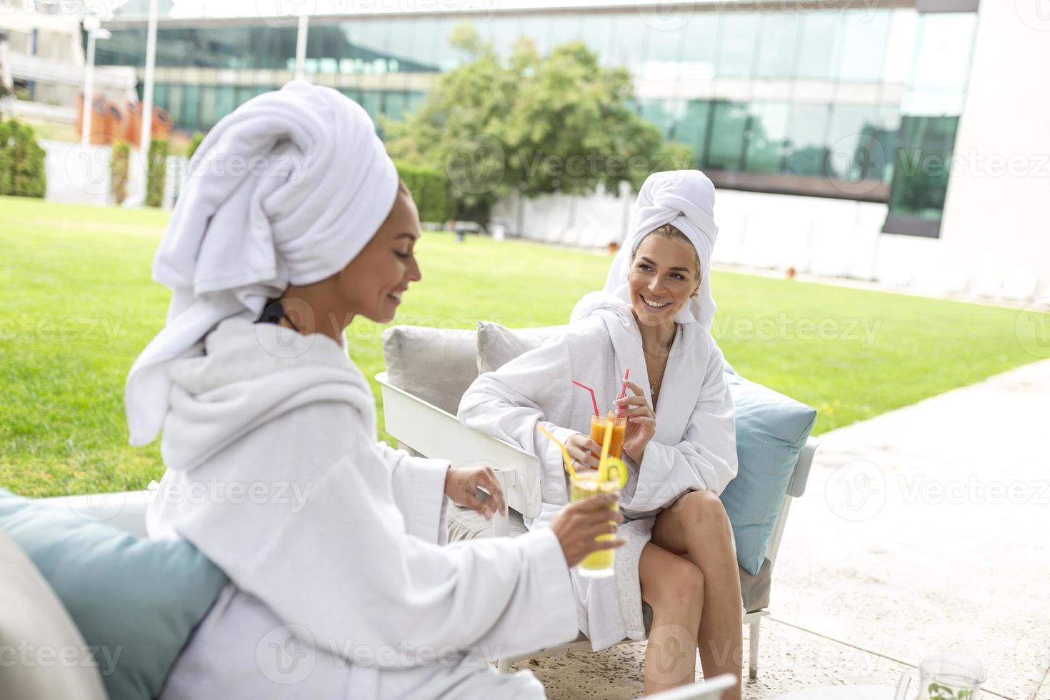 felices jóvenes hermosas mujeres disfrutando de la diversión después de los procedimientos de spa juntas en un hotel de lujo, usando toallas en la cabeza y albornoces. foto