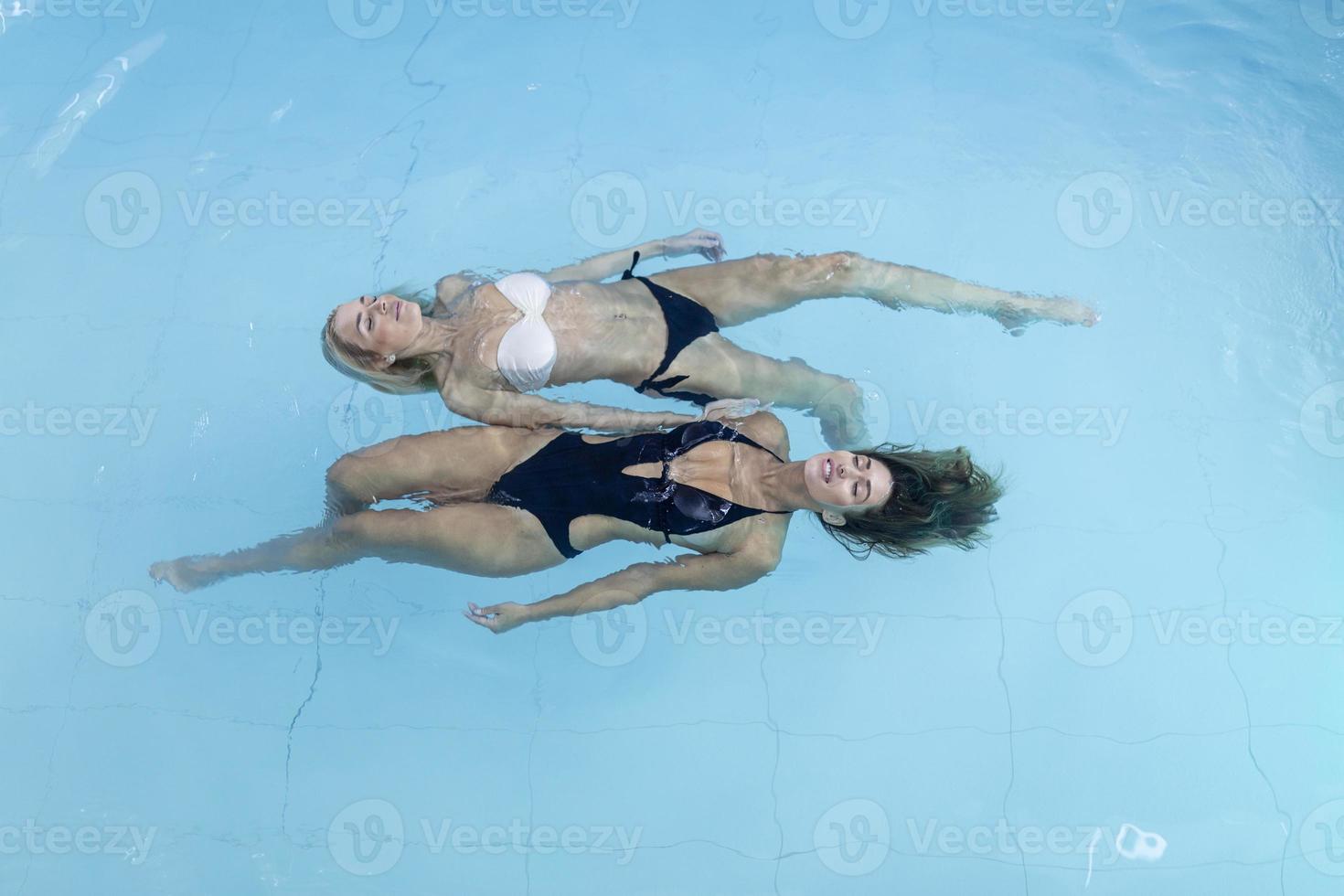 Young women relaxing and enjoying on health spa poolside. They are floating on water in swimming pool, wears bikini and looks beautiful, serene and carefree. photo